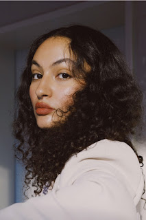 Profile picture of Anja Saleh, a light-skinned woman of colour. She sits sideways to the camera and turns her head to look directly in the lense. She has a serious expression on her face.