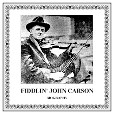 John Carson wearing a suit and holding a fiddle with a hat on his head. Black and white picture