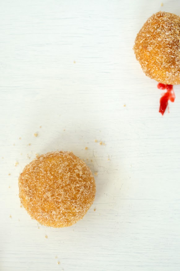 Flaumige Krapfen mit orangefarbenem Teig, roter Füllung und in Kristallzucker gewälzt.