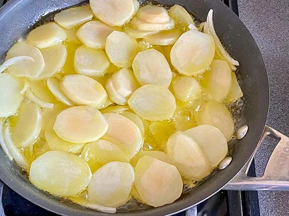 Potatoes and onions cooking in a frying pan with oil.