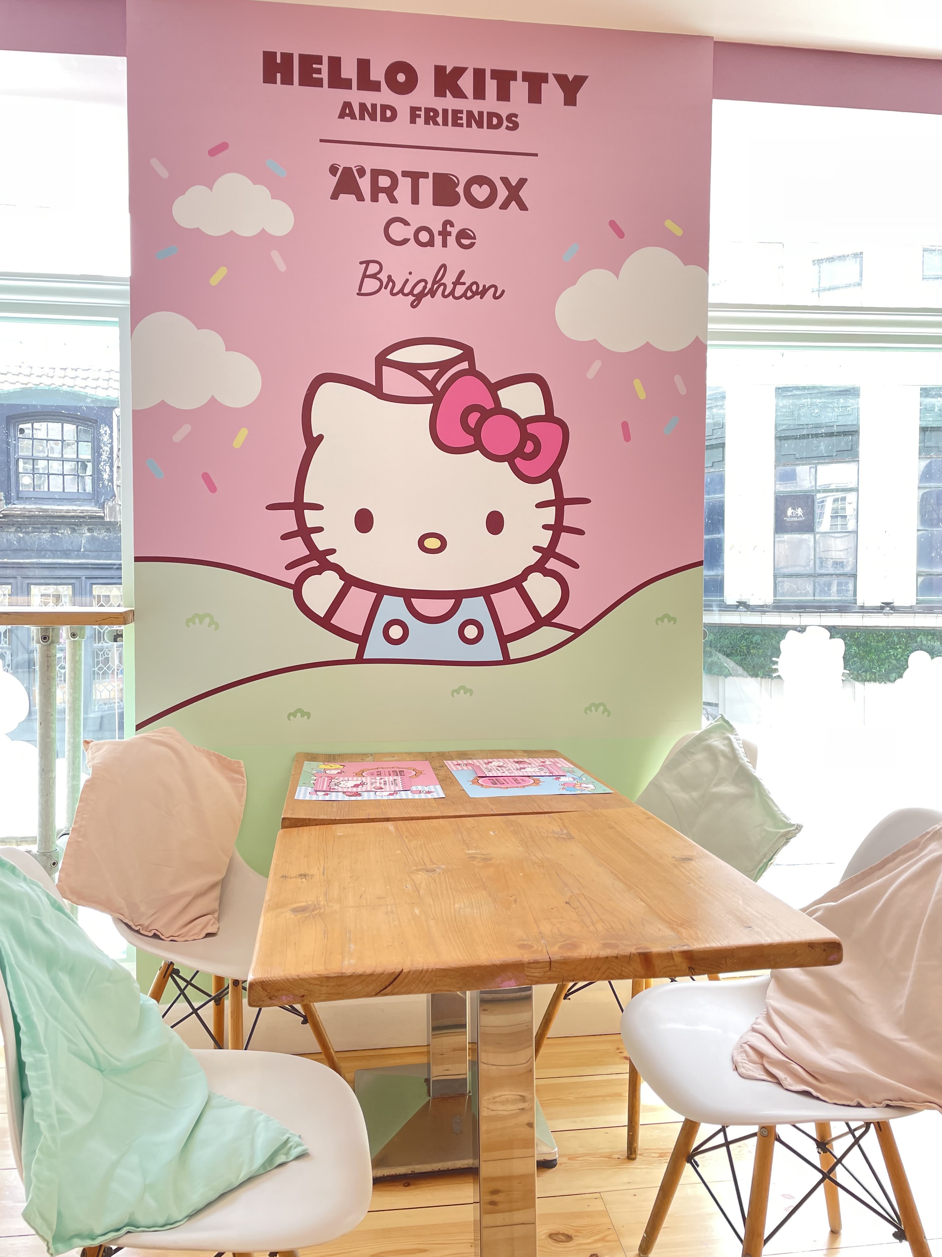 A four seater table in front of a Hello Kitty wall decal which reads, 'Hello Kitty and Friends Artbox Cafe Brighton'