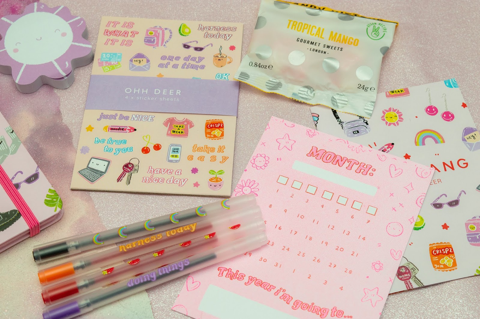 A flat lay of stickers, four pens, a postcard and sweets.