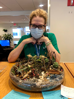 Roxanne wearing a mask and green shirt, standing behind the fairy garden.