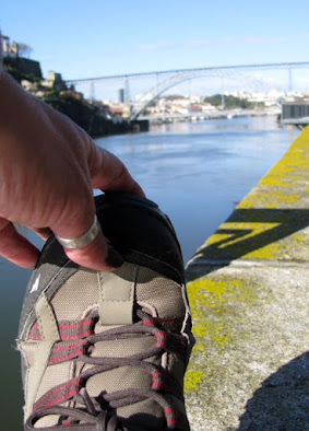 Uma mão fazendo alongamento em pé com calçado de caminhada com o rio Douro e a ponte Luiz I ao fundo