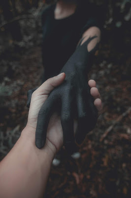 Dos personas dándose la mano en un bosque, una con la mano limpia y otra con la mano pintada de negro con un diseño atemorizante