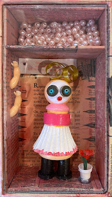 small assemblage with doll, beads, plastic flower