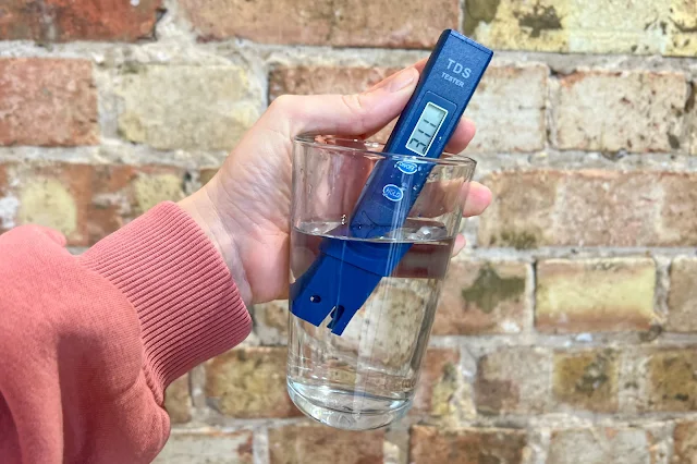 A glass of water with a TDS tester in reading 311