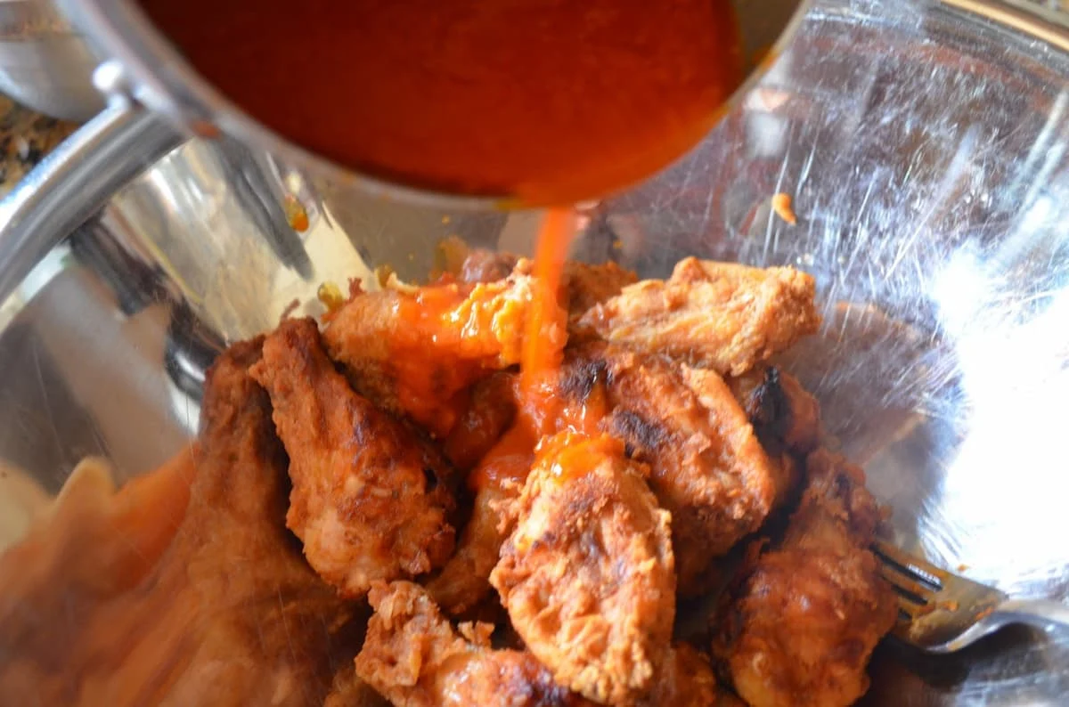 Hot Sauce with butter being drizzled over Fried Hot Wings in a large stainless steel bowl.