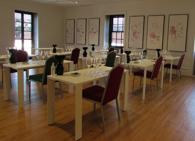 Uma sala com várias janelas e pinturas na parede mesas e cadeiras e vários copos para provas de vinhos