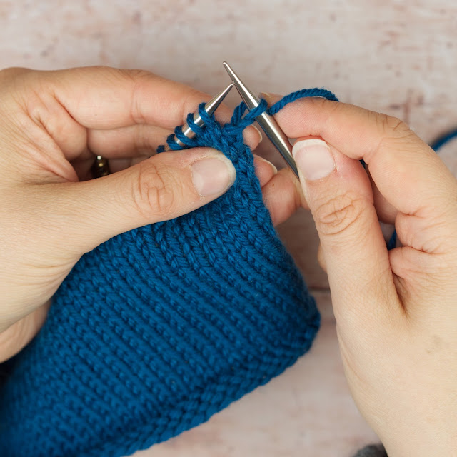 hands holding blue knitting and one stitch knitted