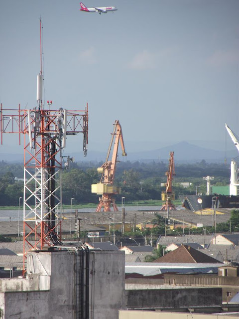 Imagem mostra avião da TAM se preparando para aterrissar no Aeroporto Internacional Salgado Filho em Porto Alegre. A foto apresenta os bairros Marcílio Dias e Centro Histórico. Edifícios e antenas de celulares escondem a bela paisagem formada pela Ilha do Pavão, pertencente ao Parque Estadual do Jacuí, e distante cadeia de morros e montanhas