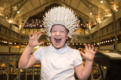 Girl wearing a large brown, spiky hat which is a replica of a porcupine fish helmet