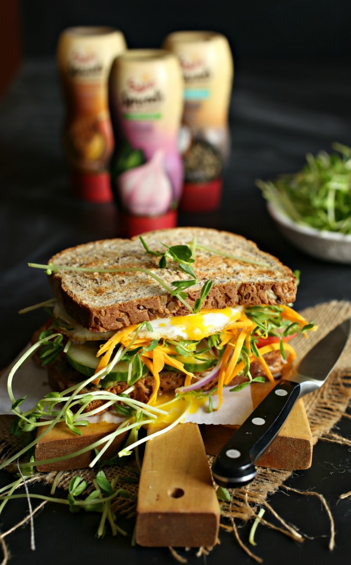 Recipe for a sandwich, dressed with hummus and filled with avocado, tomato, cucumber, carrots and a fried egg.