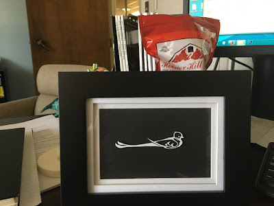 A small black picture frame with a white double mat, a black background, and a finely detailed, stylized silhouette in white of a flycatcher.