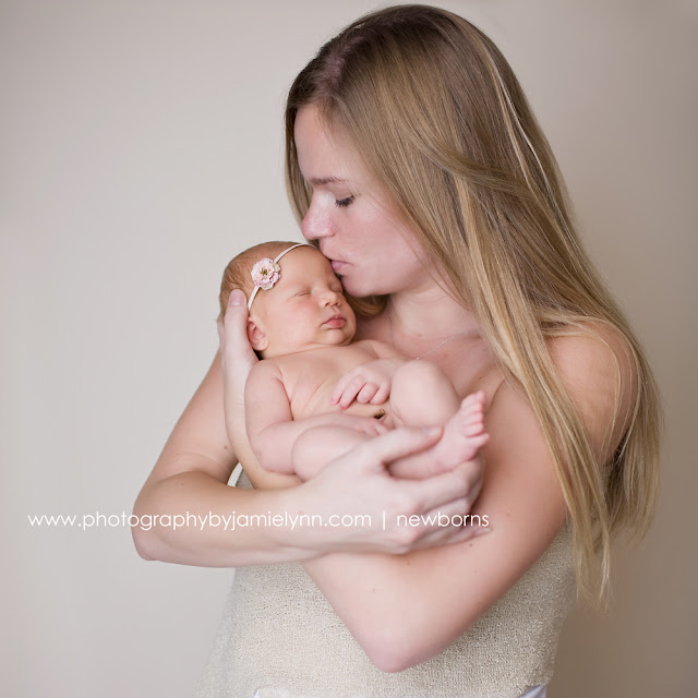 studio portrait newborn baby girl wearing small flower headband with mommy knit wrap cream backdrop