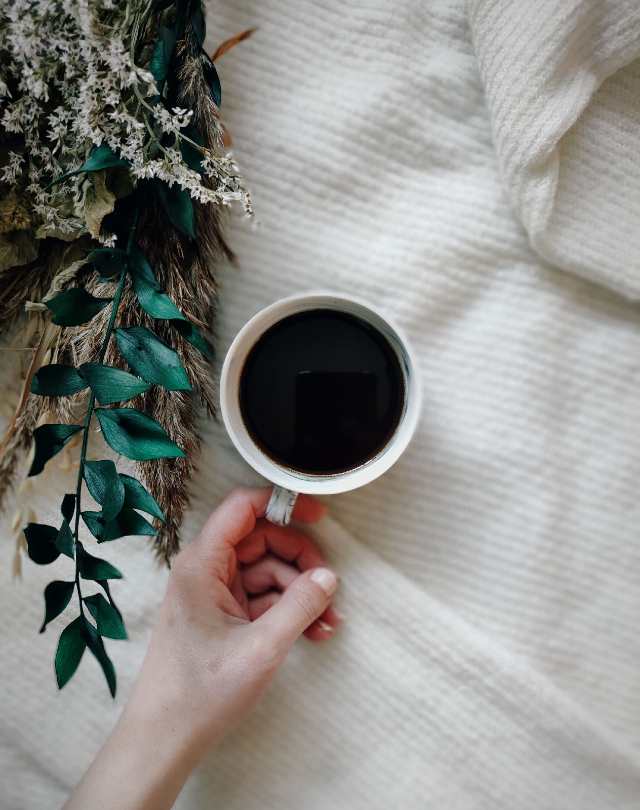 cup of black coffee next to a bouquet of dried flowers