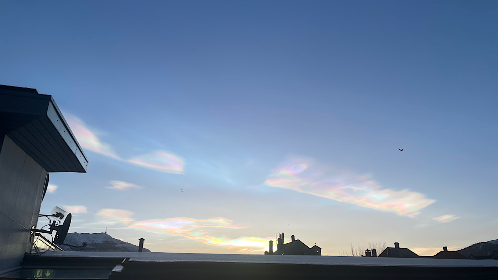 Iridescent nacreous clouds visible above rooftops in Bergen in December. The clouds have a pearlescent or rainbow quality