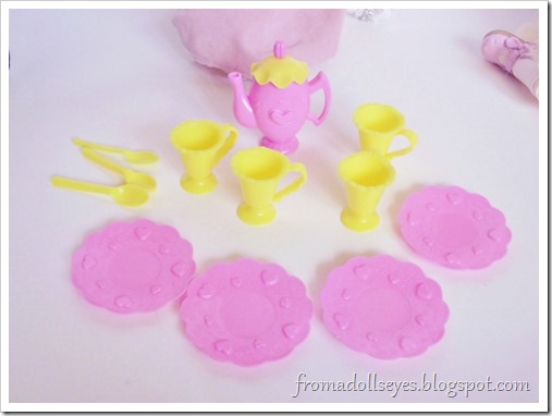 The set of plastic dishes, neatly arranged to serve tea for up to four dolls.