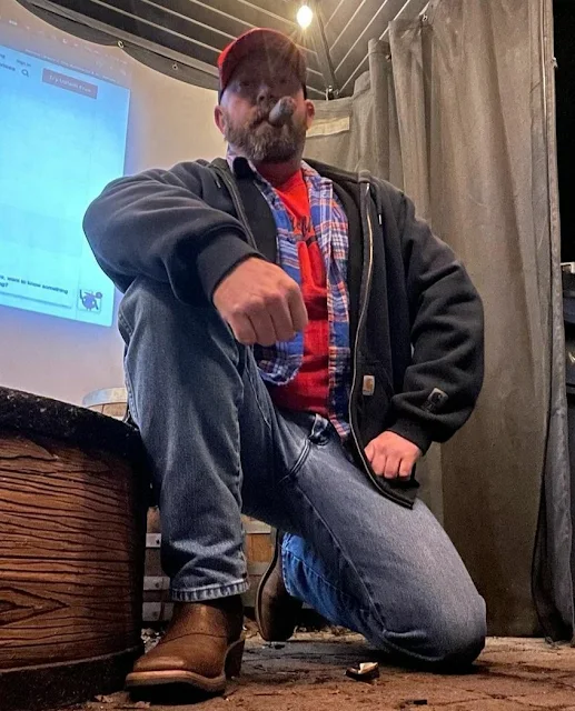 C 2/2 Country fellow kneeling down wearing flannel jeans and showing off cowboy boots smoking a cigar