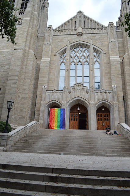 Downtown church with a pride flag hanging from its door.