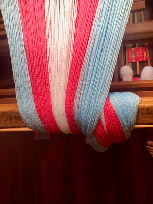 A close up of a wide, thick warp in the colours of the trans pride flag, wrapped once around the cloth beam of a floor loom.