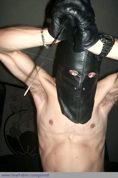 From chest up leather hooded and gloved man holding knife has tattoos