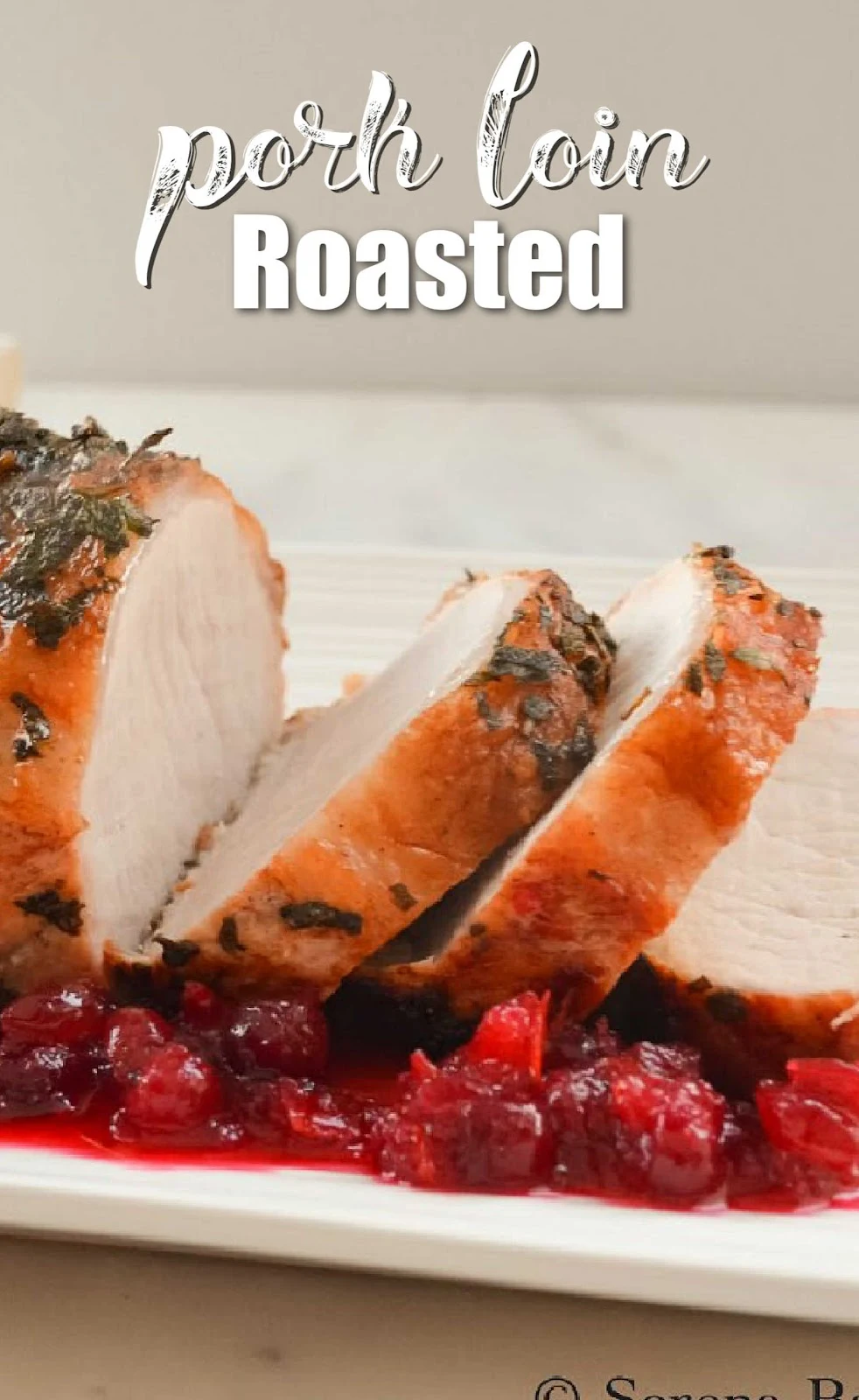 A side shot of a Pork Loin Roast on a white serving tray with Cranberry Sauce along the edge. White text at the top of photo Pork Loin Roast.