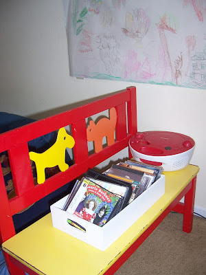 A red and yellow toddler bench with a radio and some CDs on it for children to play with