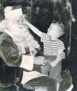 Thomas Kraemer sitting on the lap of Santa Claus pointing to his bushy eyebrows circa 1950s