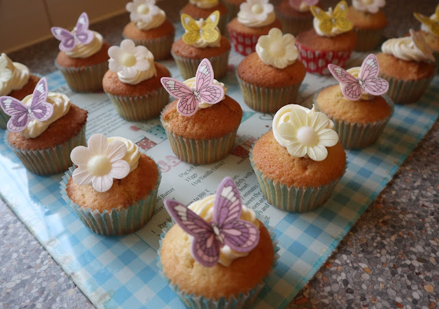 Rows of cupcakes with white frosting and decorations of butterflies and flowers