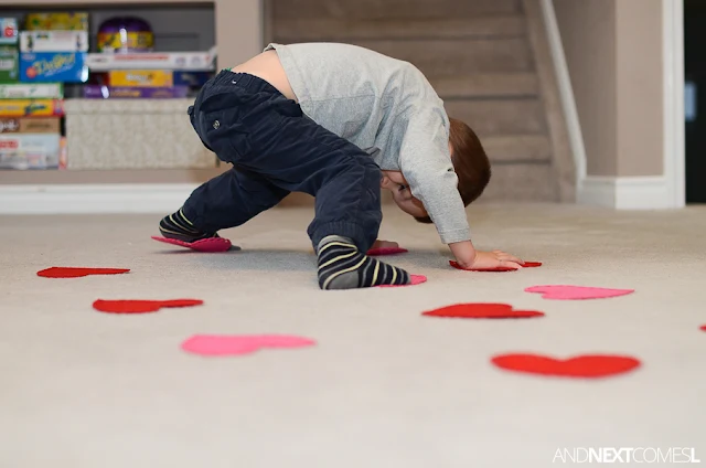 Child with hands and feet on red and pink felt hearts as part of a Valentine's Day gross motor activity