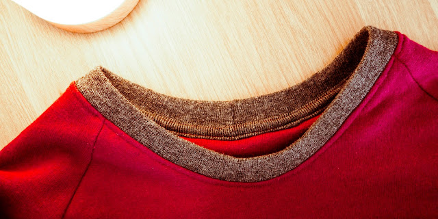 Close-up of the ribbed grey neckline on the red sweater, with matching grey binding on the inside back neck.