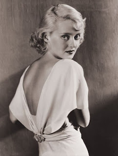 Vintage black and white photo of Bette Davis wearing a white dress with a low cut back.