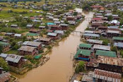 This image shows a city in Kenya located on the banks of a river. The river meanders through the city, dividing it into two parts. The city consists of houses, buildings and other structures that are located along the river and on the slopes of the hills. The city also has green areas such as parks and gardens.