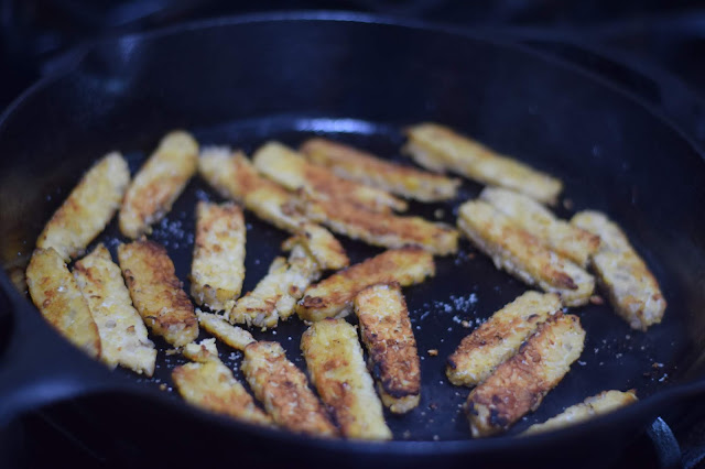 The sliced tempeh browned in a pan on the stove. 