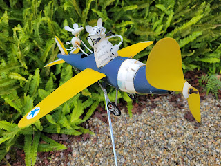 Metal lawn ornament of single-propeller airplane (blue fuselage with yellow wings) piloted by a cat & mouse