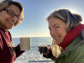 two women on rocks by sea driving coffee out of mud and thermos.