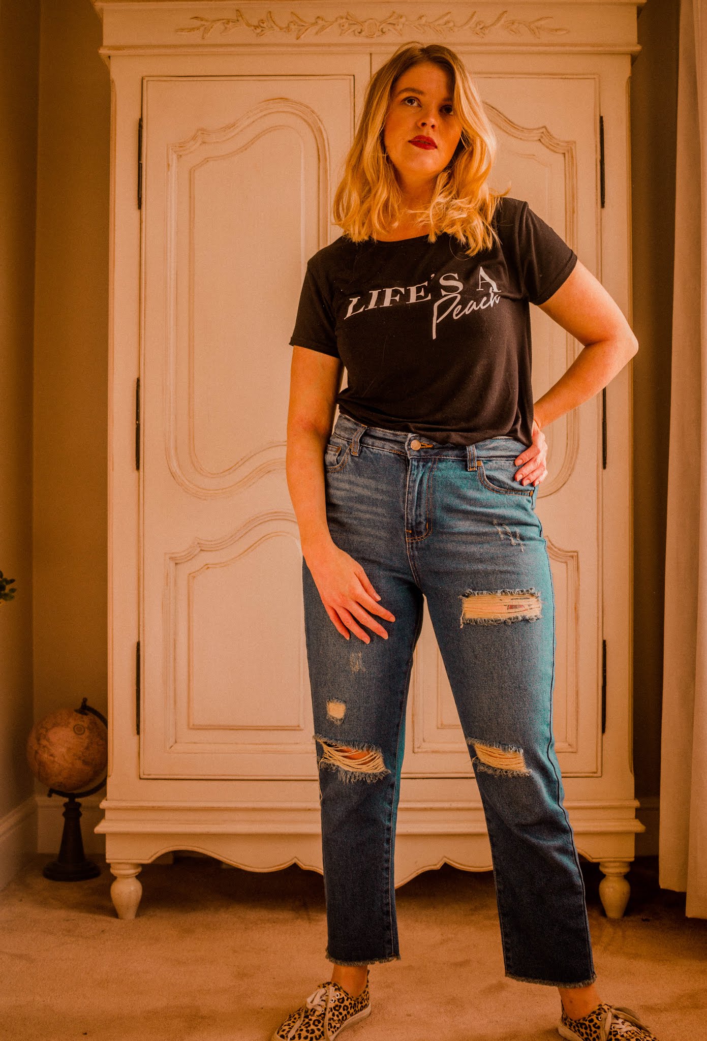 blonde girl wearing femme luxe outfit. Casual blue ripped denim high waisted jeans and black and white printed graphic tee