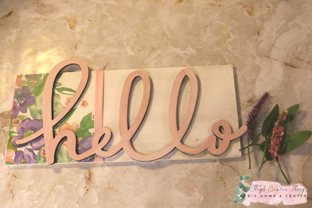 Hanging wooden hello sign with artificial flowers and decorative floral design