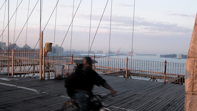 A cyclist crosses Brooklyn Bridge in the early morning sun.