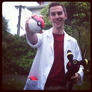 Josh, holding a Pokeball and a toy Pokemon, wearing a lab coat and a big smile.