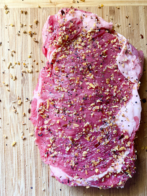 Ribeye steak on wooden cutting board topped with steak seasoning
