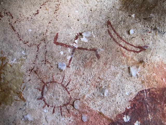 Red ochre rock painting with swastika, crescent moon, and sun.