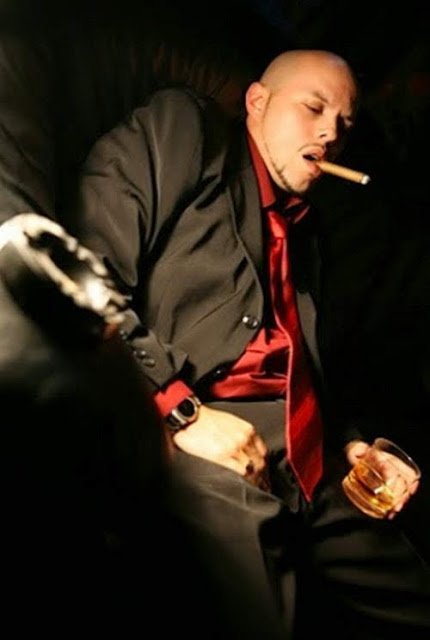 Handsome bald guy in suit kicks back smoking a cigar.