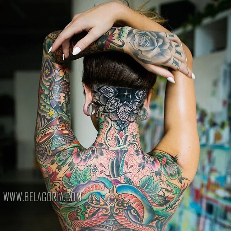 mujer de espaldas con bandana, lleva la espalda entera tatuada, en el centro un tatuaje de daga con tela de araña