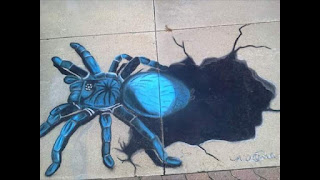 A 4'x8' sidewalk chalk drawing by Melanie Cable of a large blue and black spider climbing out of a black hole.
