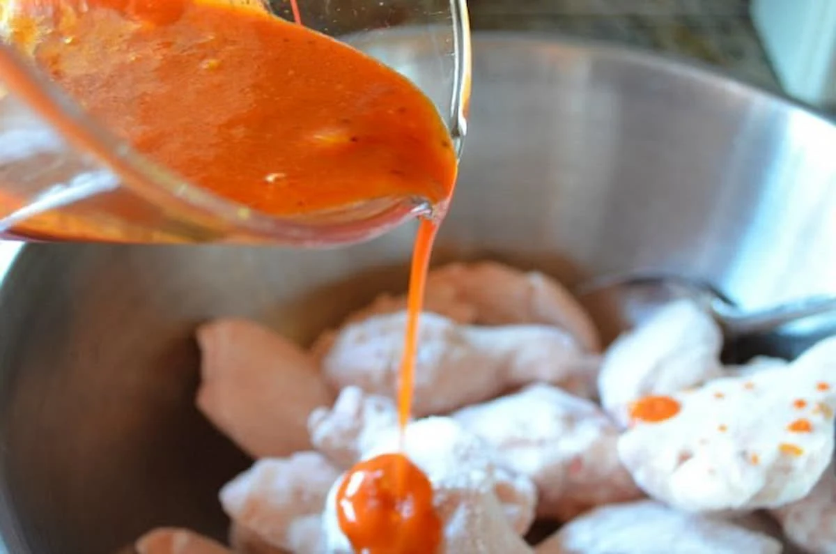 Baked Hot Wing sauce being poured over Chicken Wing Pieces.