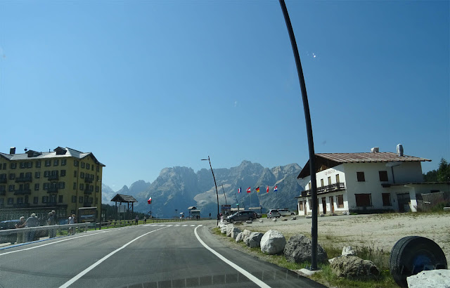 Gelb-braunes Haus, Bergmassive, blauer Himmel, Flaggen, Fahrbahn auf der Großen Dolomitenstraße in Südtirol