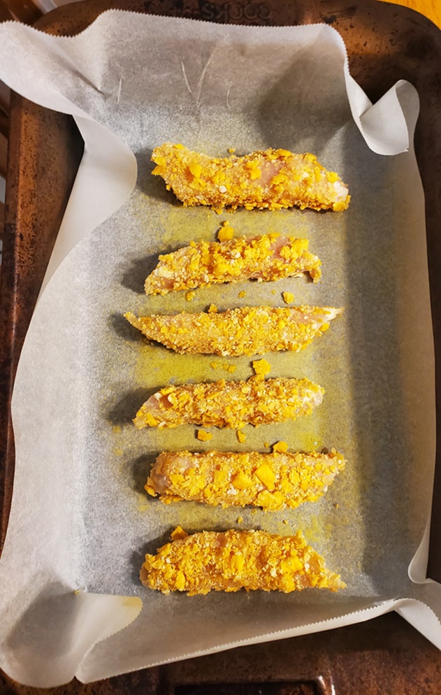 chicken fingers ready to be baked coated with cheese cracker crumbs