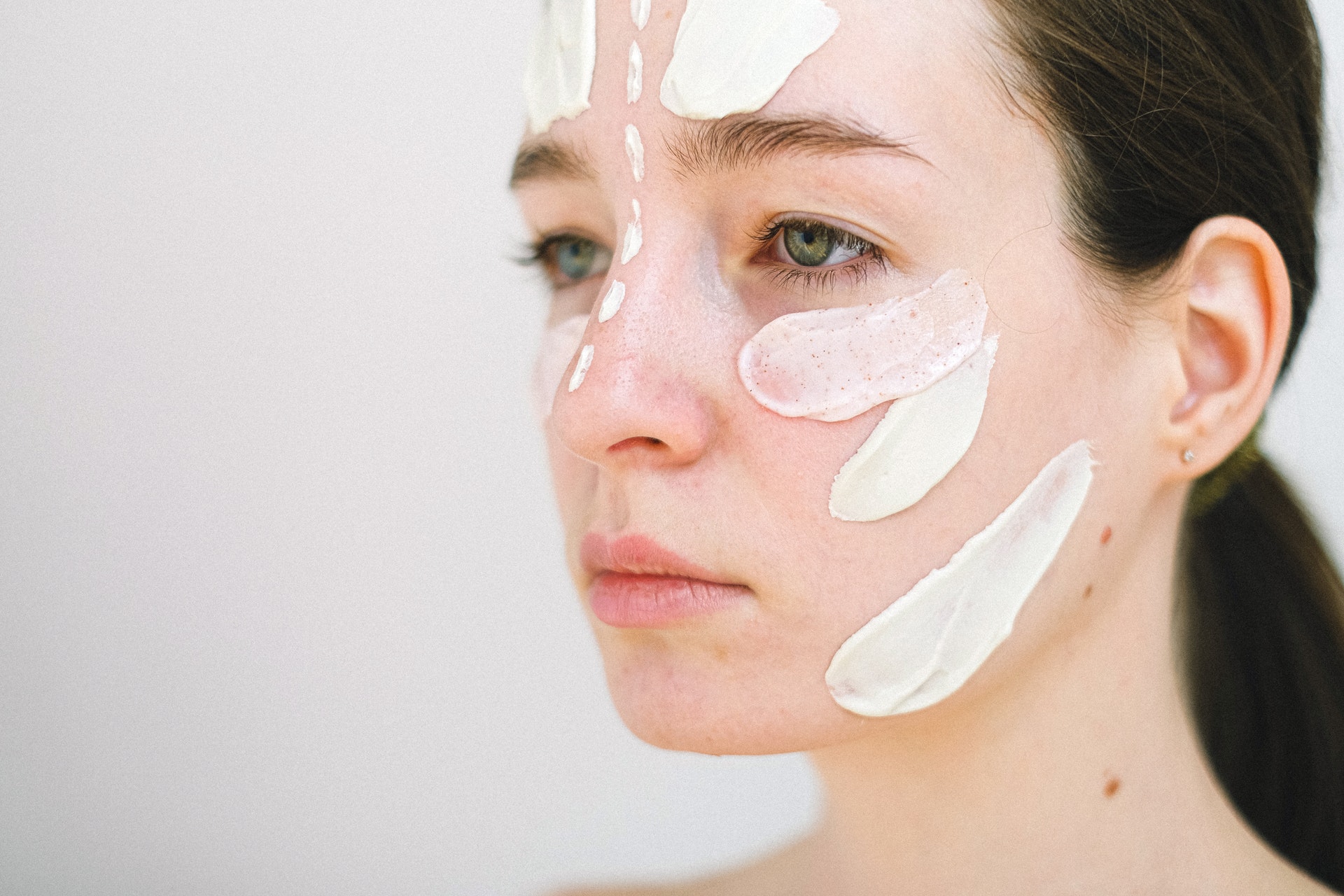 Side view of crop female model spreading white cream on face during skincare procedure on white background. Check the content of the screen you are using. Photo by Anna Shvets from Pexels